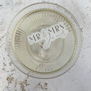 May include: A clear glass cake stand with a textured surface. The stand has a sticker on it that says "MR & MRS Jones".