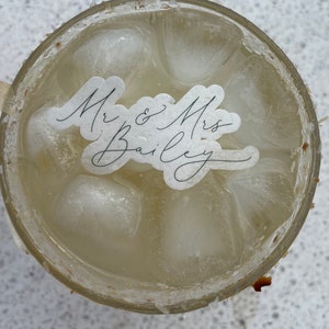 May include: A clear glass with ice and a white sticker that says "Mr. & Mrs. Bailey" on it.