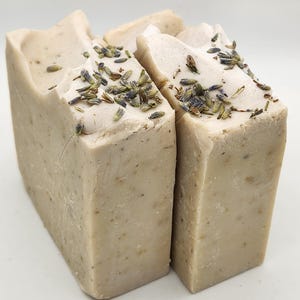 Puede incluir: Dos barras de jabón hechas a mano de color marrón claro con motas de flores de lavanda secas en la parte superior.