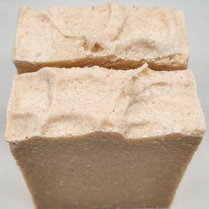 May include: Two bars of handmade soap with a light brown colour and a rough, textured surface. The soap is made with natural ingredients and is perfect for sensitive skin.