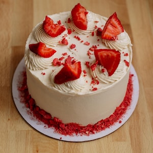 May include: A white cake frosted with white frosting and decorated with fresh strawberries and freeze-dried strawberries.