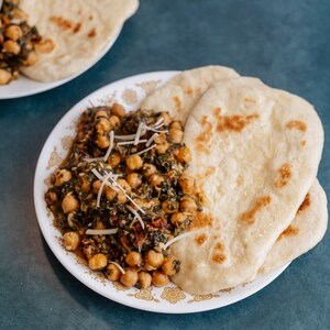 Może przedstawiać: Talerz z zielonym curry ze szpinaku i ciecierzycy z trzema płaskimi chlebkami. Curry posypane startym serem.