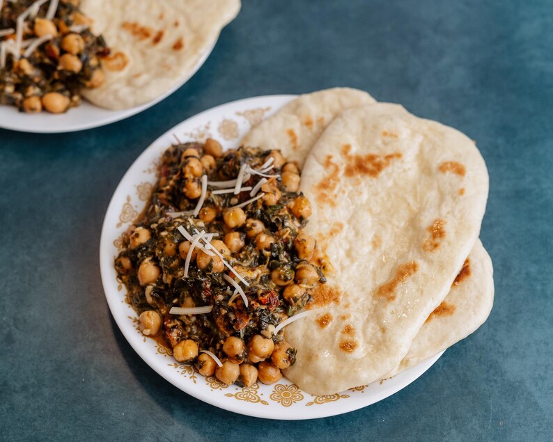 Może przedstawiać: Talerz z zielonym curry ze szpinaku i ciecierzycy z trzema płaskimi chlebkami. Curry posypane startym serem.