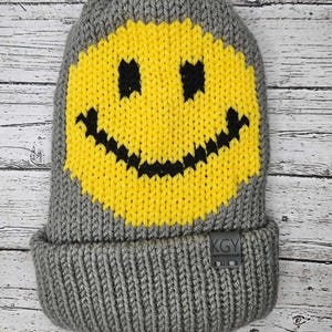 May include: Gray knitted beanie with a yellow smiley face design and a black "KGY" logo tag.
