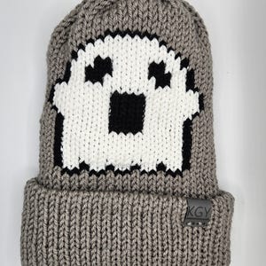 Pode incluir: Boné de malha cinzento com um design de fantasma pixelado branco e preto. O boné tem uma aba dobrável e uma etiqueta preta com o texto "KGY" no lado.