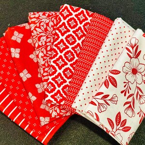 May include: A collection of folded fabric napkins in various patterns. The napkins feature red and white designs, including stripes, floral, geometric, and dotted patterns. The napkins are arranged in a fan shape, showcasing the variety of designs.