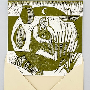 May include: An olive green and white linocut print showing a person weaving baskets. The image includes a crescent moon, a vase, and a basket. The print is presented inside a cream-coloured envelope.