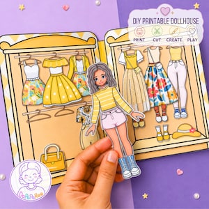 Op de afbeelding: Een DIY printbare papieren poppenhuisset met een kledingkast met twee deuren vol diverse geïllustreerde outfits, waaronder jurken, tops en broeken op hangers. Een papieren pop met golvend haar wordt voor de open kast gehouden.