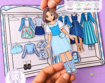 Könnte beinhalten: Ein DIY-Bastelset mit einer Papierpuppe, die braune Haare hat und ein blaues Kleid sowie Stiefel trägt. Das Set enthält einen Kleiderschrank-Hintergrund mit verschiedenen Papierkleidungsstücken wie Jacken, Röcken und Kleidern in Blautönen.