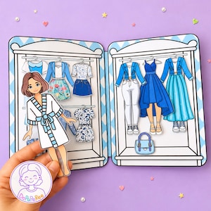 May include: A paper doll set featuring a character in a white robe and a two-door closet filled with various outfits, including blue jackets, skirts, dresses, and pants. The set includes a small blue handbag and a circular logo labeled DoPaPeRee.