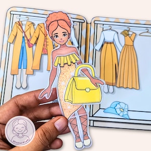 Op de afbeelding: Een papieren pop met een gele jurk en bijpassende handtas. De pop houdt de handtas vast en staat voor een kledingkast met gele jassen en jurken. De pop heeft oranje haar en draagt witte schoenen.