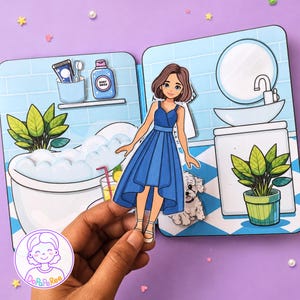 May include: A paper doll set featuring a cartoon character in a blue dress standing in a bathroom scene. The scene includes a bathtub with bubbles, a sink, a mirror, a potted plant, and a small white dog. The text DoPaPeRee is visible in a logo.