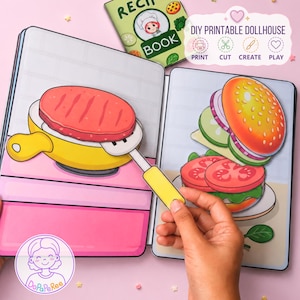 Könnte beinhalten: Ein DIY-Puppenhaus-Buch zum Ausdrucken mit einer gelben Pfanne, einem roten Burger-Patty, einem Pfannenwender und einer Burger-Illustration. Das Buch enthält ein Rezeptbuch-Cover und den Text DIY PRINTABLE DOLLHOUSE PRINT CUT CREATE PLAY.