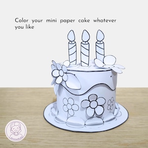 Puede incluir: Una tarta de papel blanca con contornos negros, con tres ilustraciones de velas y dise&ntilde;os florales. El texto "Color your mini paper cake whatever you like" est&aacute; visible. La tarta est&aacute; dise&ntilde;ada para colorear.