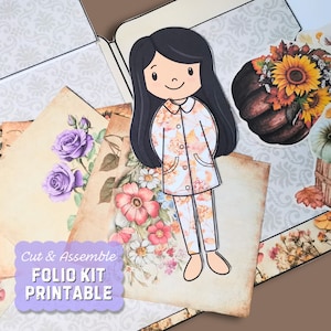 Pode incluir: Kit de fólio imprimível com um design para cortar e montar, apresentando uma menina com um vestido estampado floral, flores e uma abóbora com um girassol no topo. O texto "Cut & Assemble FOLIO KIT PRINTABLE" está no canto inferior esquerdo da imagem.