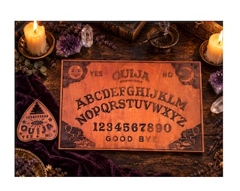 May include: A rectangular wooden Ouija board featuring the alphabet, numbers 0-9, the words YES, NO, and GOOD BYE, and a sun and moon design. A matching wooden planchette with an eye graphic and the word OUIJA is positioned to the left.