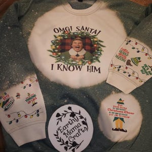 May include: A green sweatshirt with a white bleach design featuring a Christmas-themed image of Buddy the Elf from the movie Elf. The text "OMG! SANTA! I KNOW HIM" is printed on the sweatshirt. The sleeves have additional Christmas-themed designs with text like "You sit on a throne of lies" and "Cotton Headed Muccins".