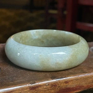 May include: A light green jade bangle bracelet with a smooth, polished surface.