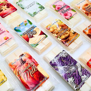 May include: A collection of rectangular wax melt bars in clear plastic packaging, each featuring a unique label with text such as Pomegranate Vanilla, Eucalyptus & Spearmint, Hawaiian Hibiscus, Sugared Cinnamon Doughnut, Sweet Strawberry, Coconut Bliss, Nag Champa, Golden Pear & Clove, Pumpkin Milk, White Sage & Lavender, and Vanilla Almond.