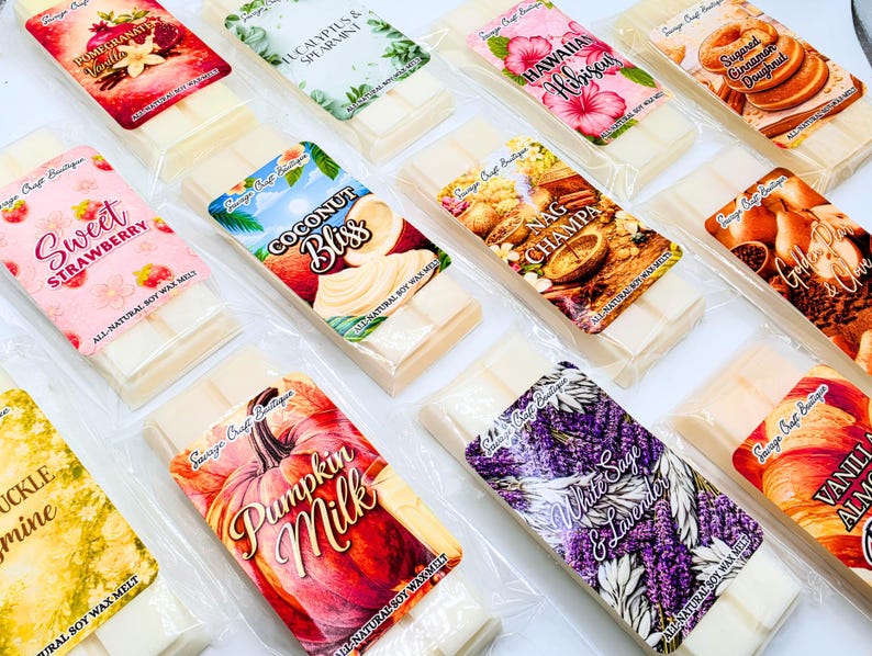 May include: A collection of rectangular wax melt bars in clear plastic packaging, each featuring a unique label with text such as Pomegranate Vanilla, Eucalyptus & Spearmint, Hawaiian Hibiscus, Sugared Cinnamon Doughnut, Sweet Strawberry, Coconut Bliss, Nag Champa, Golden Pear & Clove, Pumpkin Milk, White Sage & Lavender, and Vanilla Almond.