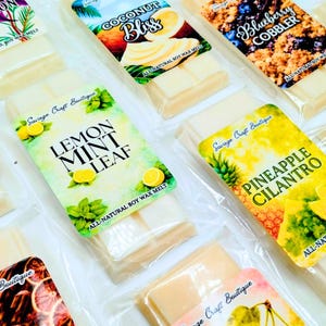 May include: A collection of rectangular soy wax melt bars in clear plastic packaging. Each bar features a colorful label with text including Lemon Mint Leaf, Pineapple Cilantro, Coconut Bliss, and Blueberry Cobbler, all marked as all-natural soy wax.