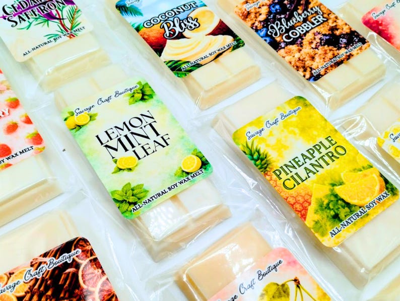 May include: A collection of rectangular soy wax melt bars in clear plastic packaging. Each bar features a colorful label with text including Lemon Mint Leaf, Pineapple Cilantro, Coconut Bliss, and Blueberry Cobbler, all marked as all-natural soy wax.