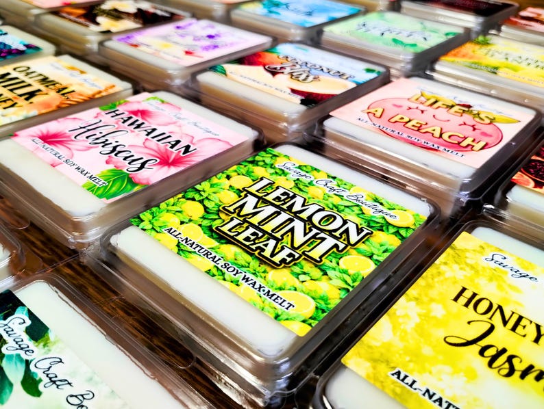May include: A collection of square soy wax melts in clear plastic containers, each featuring a colorful label with text such as Lemon Mint Leaf, Hawaiian Hibiscus, Life's A Peach, and Honey Jasmine, showcasing various fruit and floral illustrations.