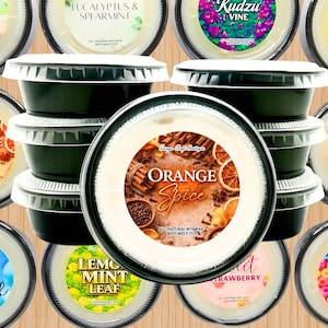 May include: A collection of round, black plastic cups filled with white soy wax melts. Each cup features a circular label with unique scent names and graphics, including Orange Spice, Serenity Spa, Eucalyptus & Spearmint, Kudzu Vine, Honeysuckle Jasmine, Cinnamon Spiced Vanilla, Just Breathe, Lemon Mint Leaf, Sweet Strawberry, and Fruit Loops.
