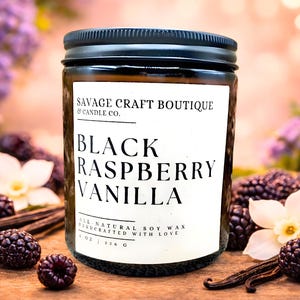 Può includere: Una candela in barattolo di vetro con coperchio nero e etichetta bianca con la scritta Savage Craft Boutique & Candle Co. Black Raspberry Vanilla. L'etichetta indica 226 g di cera di soia naturale. Circondata da more e fiori di vaniglia.