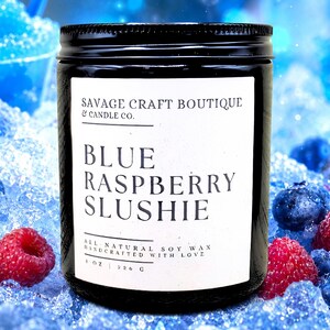 May include: A black glass candle jar with a white label featuring the text Savage Craft Boutique & Candle Co. Blue Raspberry Slushie, All Natural Soy Wax, Handcrafted With Love, 8 oz | 226 g, set against a background of blue ice and berries.