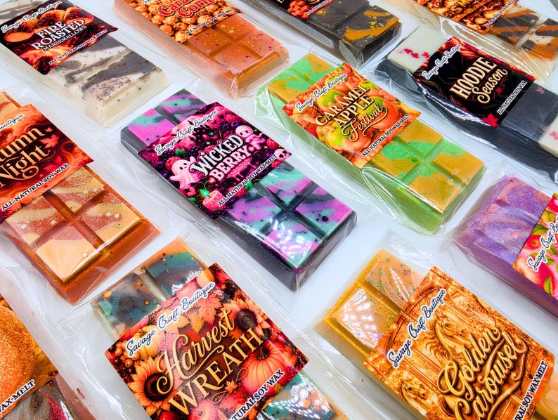 May include: A collection of rectangular soy wax melts in clear plastic packaging, each featuring a unique label with names like Wicked Berry, Caramel Apple Festival, Harvest Wreath, and Golden Carousel, showcasing various colorful wax patterns.