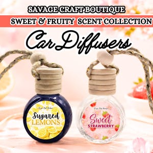 Puede incluir: Dos difusores de coche de la colección Sweet & Fruity Scent. Uno es una botella azul oscuro con la etiqueta "Sugared Lemons" y el otro es una botella transparente con la etiqueta "Sweet Strawberry". Ambos tienen tapas de madera y cordones colgantes. El fondo incluye limones y fresas.