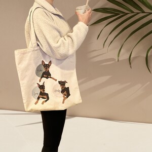 Pu&ograve; includere: Una borsa tote in tela bianca con tre illustrazioni di cani neri e marroni. I cani si chiamano "Baby", "Louis" e "Shady".