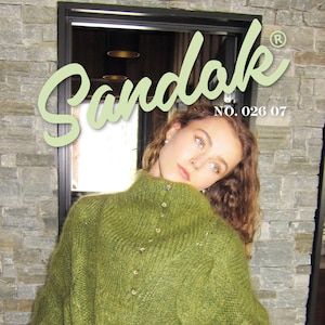 Könnte beinhalten: Ein grüner Zopfstrickpullover mit hohem Kragen und Knopfdetails. Der Pullover ist mit "Sandak" mit der Nummer "026 07" und "Cable Sweater Größe 1-3" gekennzeichnet. Das Model trägt den Pullover.