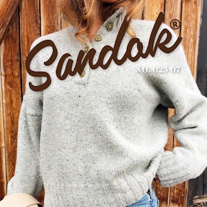 Puede incluir: Un suéter gris claro con cuello abotonado y mangas largas. El suéter tiene un tejido texturizado y se combina con unos vaqueros azules. La palabra "Sandak" se muestra en una fuente marrón. También se ve el texto "Sweater 3" y "Size XS-XXL".