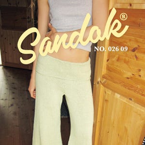 May include: Light green knit pants with a wide leg, paired with a gray tank top. The pants have a high waist and are labeled "PANTS 2" with sizes XS-XXL. The word "Sandak" is written in a cursive font.