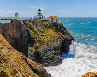 May include: A coastal scene featuring a white lighthouse with a black and green lantern room atop a rocky cliff. A suspension bridge connects to the lighthouse. The ocean waves crash against the rocks under a blue sky.