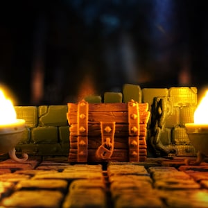 Könnte beinhalten: Eine Holzkiste mit Metallverzierungen steht in der Mitte einer steinernen Dungeon-Kulisse. Zwei leuchtende Laternen erhellen die Szene.