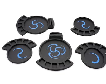 May include: Five black plastic paint palettes with blue swirl designs. Each palette has a circular well in the centre and a semi-circular row of smaller wells around the edge.