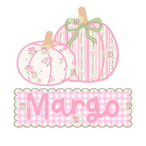 Op de afbeelding: Twee decoratieve pompoenen met bloemen- en streepmotieven en een groene strik. De pompoenen zijn roze en wit met een lichtbruine steel. Onder de pompoenen staat de naam "Margo" in roze letters op een roze en witte geruite achtergrond.
