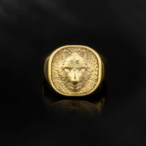 May include: A gold ring with a wolf head design. The ring is square shaped and has a textured surface.