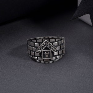 Può includere: Un anello d'argento con un motivo a mattoni e un design geometrico al centro.