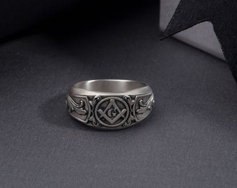 May include: A silver ring with an engraved Masonic symbol, featuring a compass and square with a 'G' in the center.