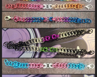 May include: A collection of colorful chainmail bracelets. Each bracelet is made of small, interlocking metal rings in various colors, including silver, gold, red, pink, blue, and purple. The bracelets have a lobster clasp closure.