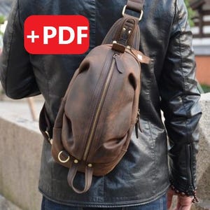 Puede incluir: Un bolso de cuero marrón cruzado con cierre de cremallera y una correa. El bolso lo lleva una persona que lleva una chaqueta de cuero negra.