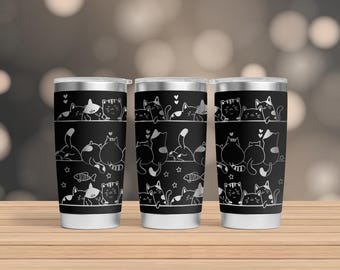 Puede incluir: Tres vasos de acero inoxidable con ilustraciones de gatos en blanco y negro. Los gatos están en varias poses, incluyendo sentados, durmiendo y jugando. Los vasos tienen un fondo negro y contornos blancos.