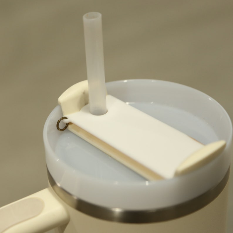 May include: White travel mug with a lid that has a straw hole and a removable white plastic insert with a hole for the straw. The mug has a silver band around the top.