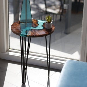May include: A round wooden table with a turquoise epoxy resin top and black hairpin legs. A small potted plant sits on the table.