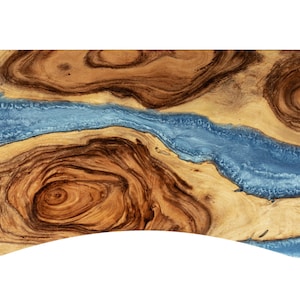 May include: A wooden serving board with a blue resin inlay. The board has a natural wood grain pattern and a curved edge.