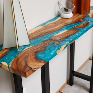 May include: A wooden console table with a turquoise blue epoxy resin top. The table has a live edge design and black metal legs.